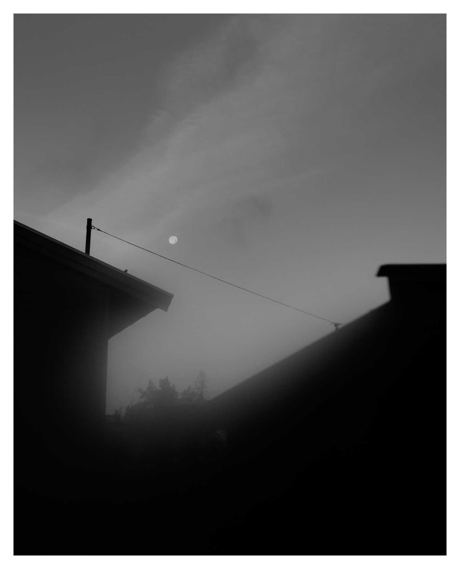 Moon above rooftops in fog, black and white