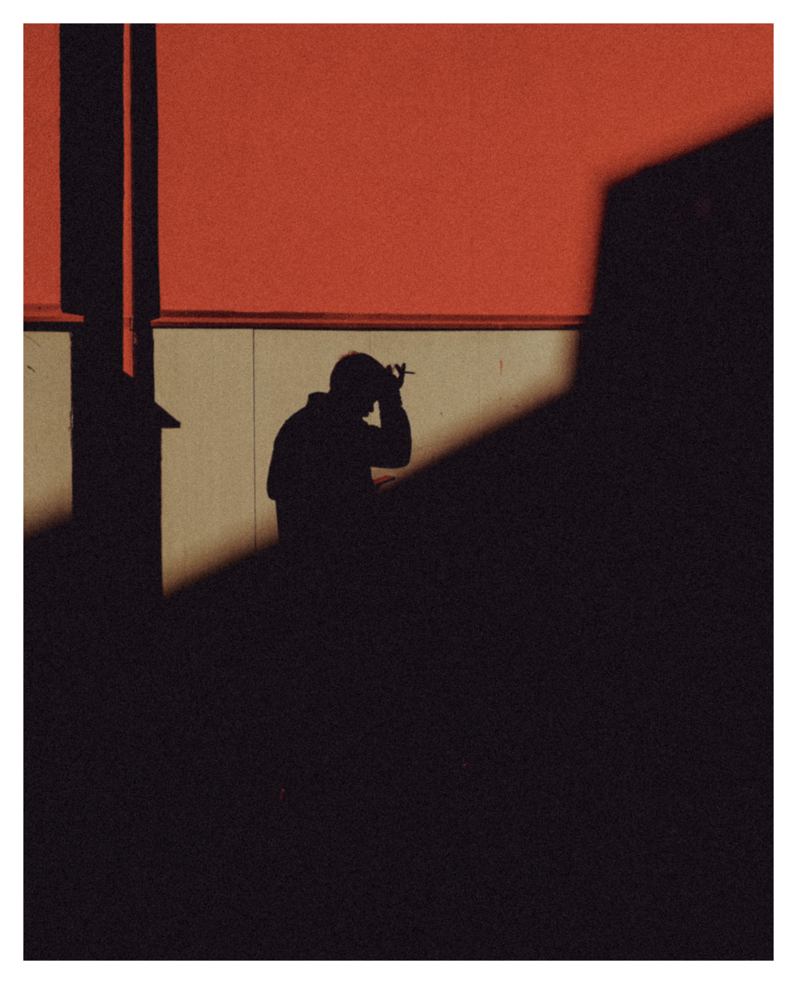 Silhouette of a person against a red wall cut by a hard diagonal shadow