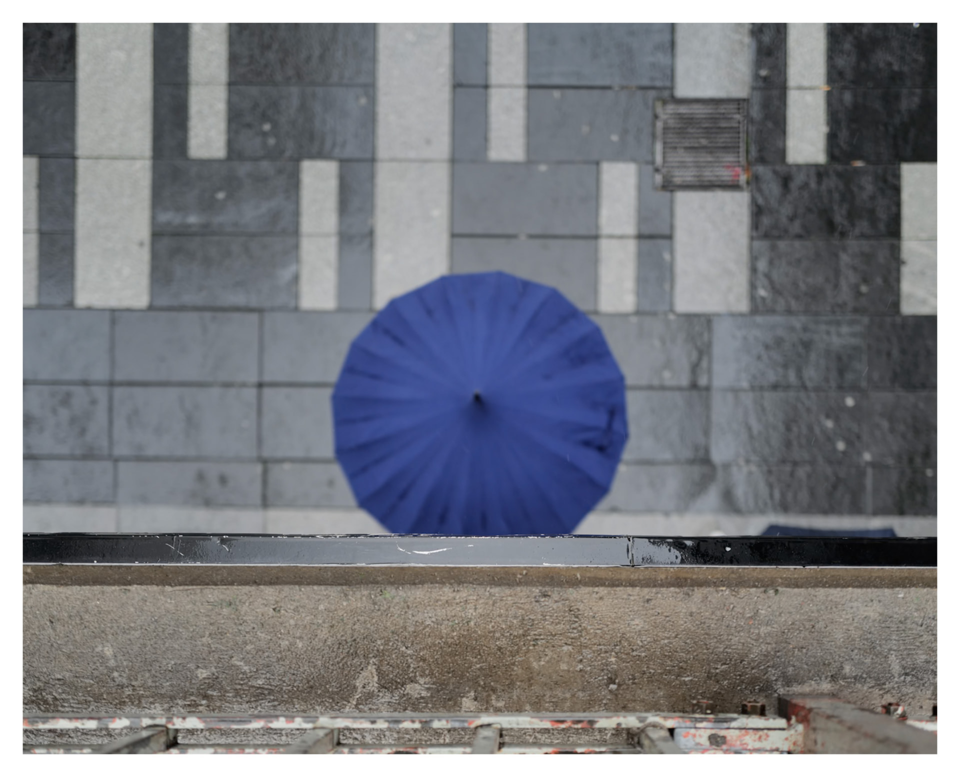 Blue umbrella seen from above against striped paving